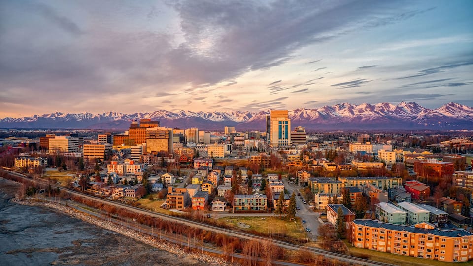 A cityscape with a prominent building and snow-capped mountains in the background.