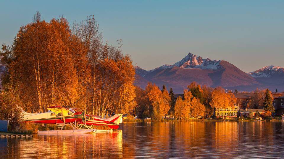 A lake with boats, autumn trees, and mountains in the background.