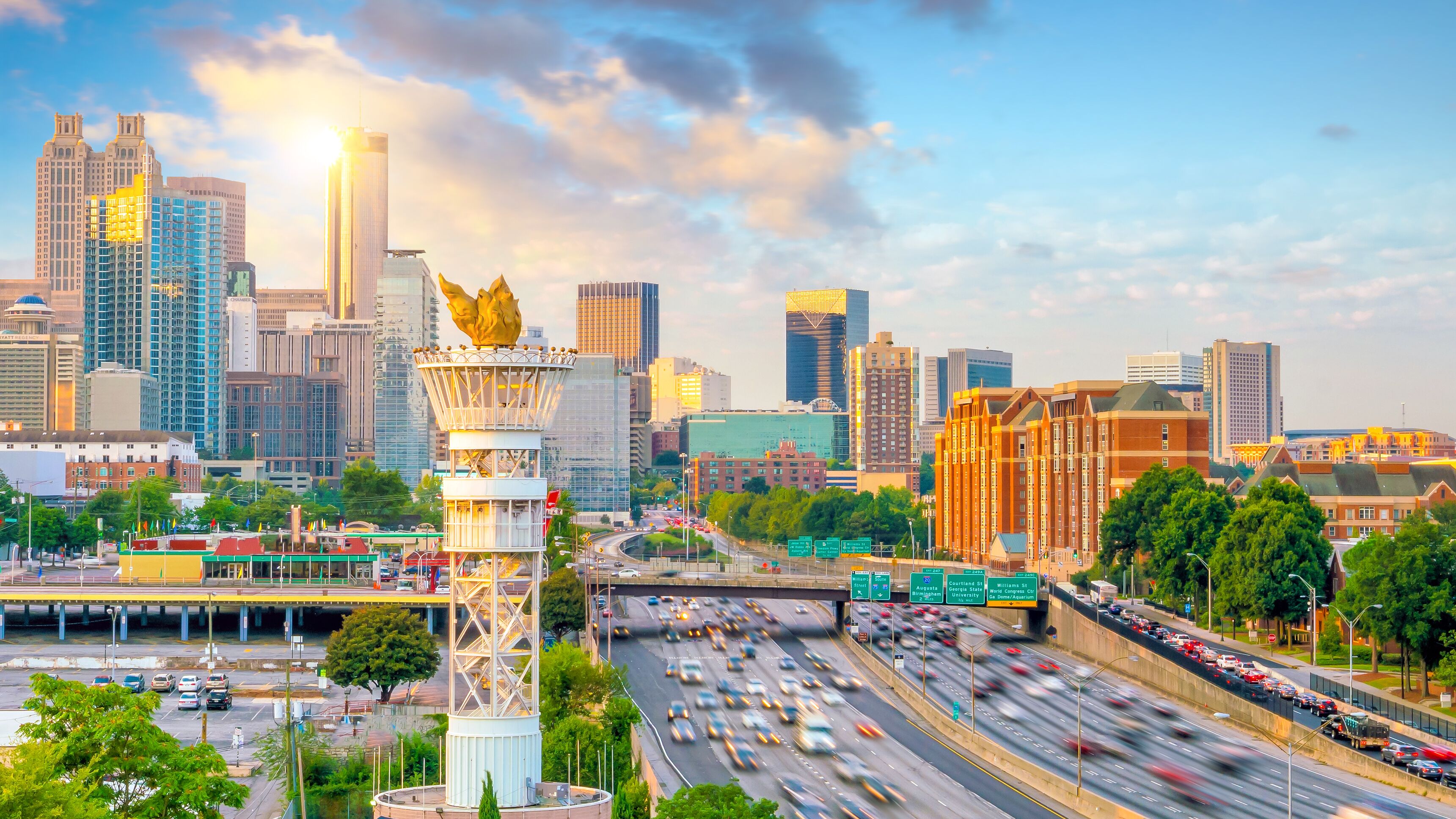 A cityscape with a prominent tower featuring a golden eagle sculpture, surrounded by modern skyscrapers and busy highways.