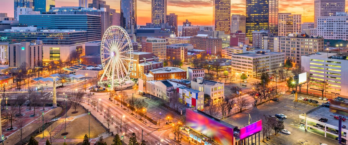A cityscape at dusk with a prominent Ferris wheel, skyscrapers, and a sunset sky.