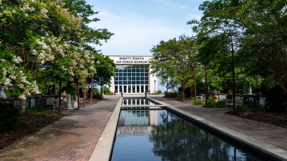 A pathway leading to the Mighty Eighth Air Force Museum surrounded by trees and a reflective water feature.
