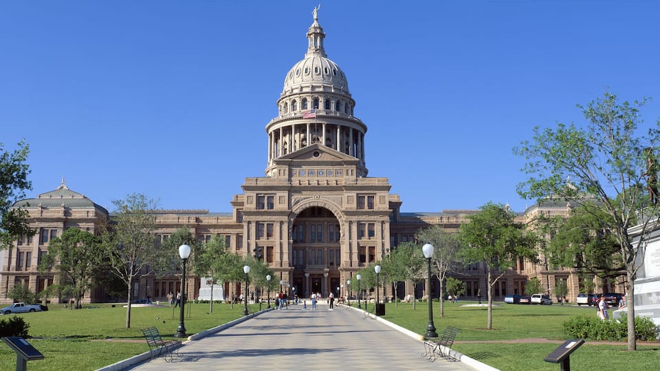A large neoclassical building with a prominent dome and columns, surrounded by statues and a central walkway.