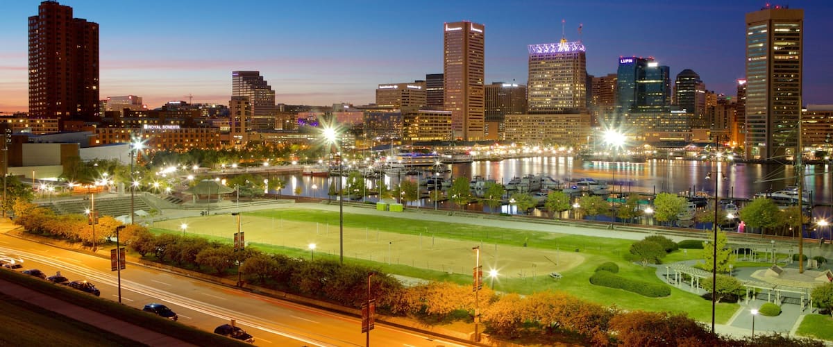 A city skyline at dusk with illuminated buildings and a river with boats.