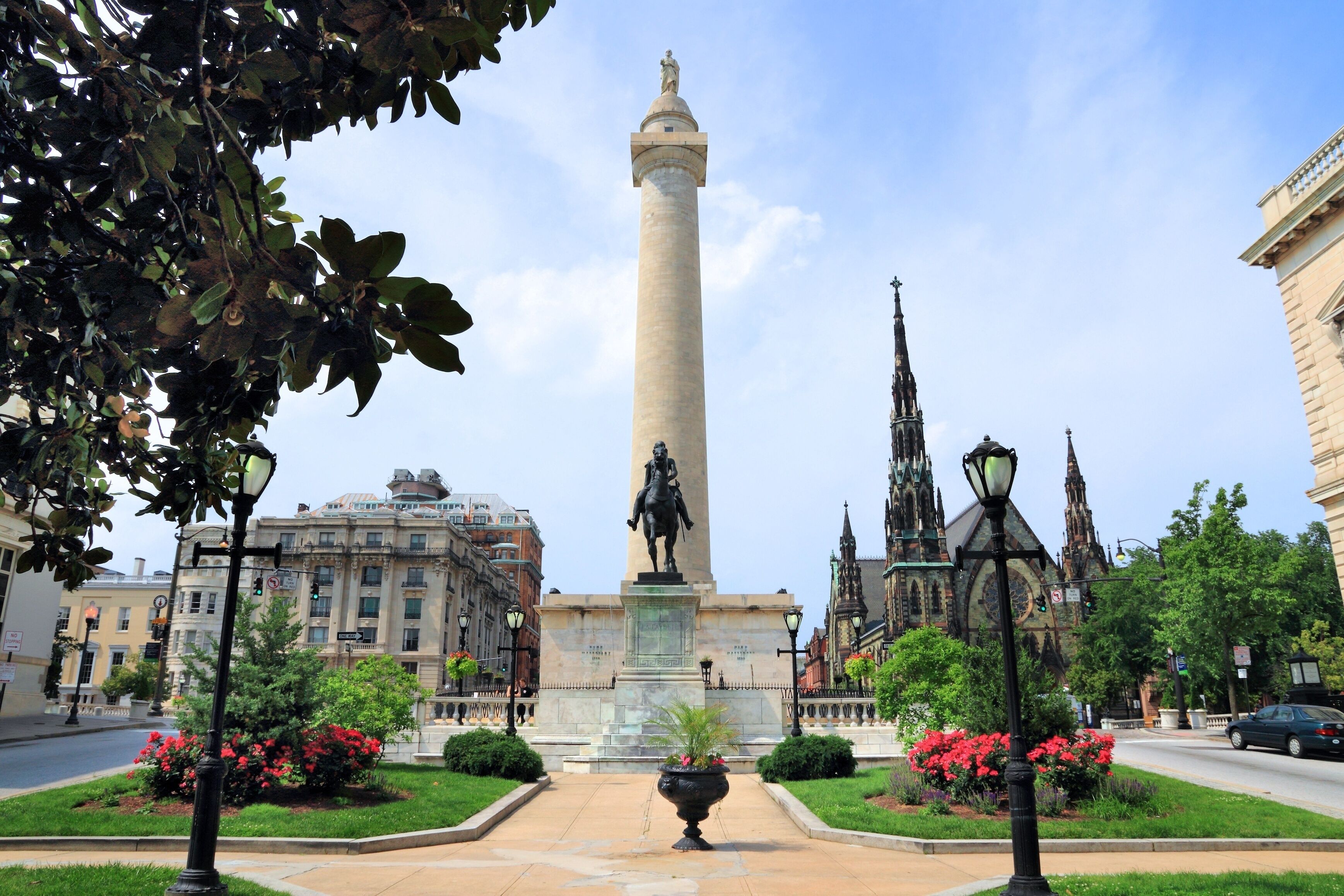 A monument with a statue, surrounded by well-maintained gardens and historic buildings.