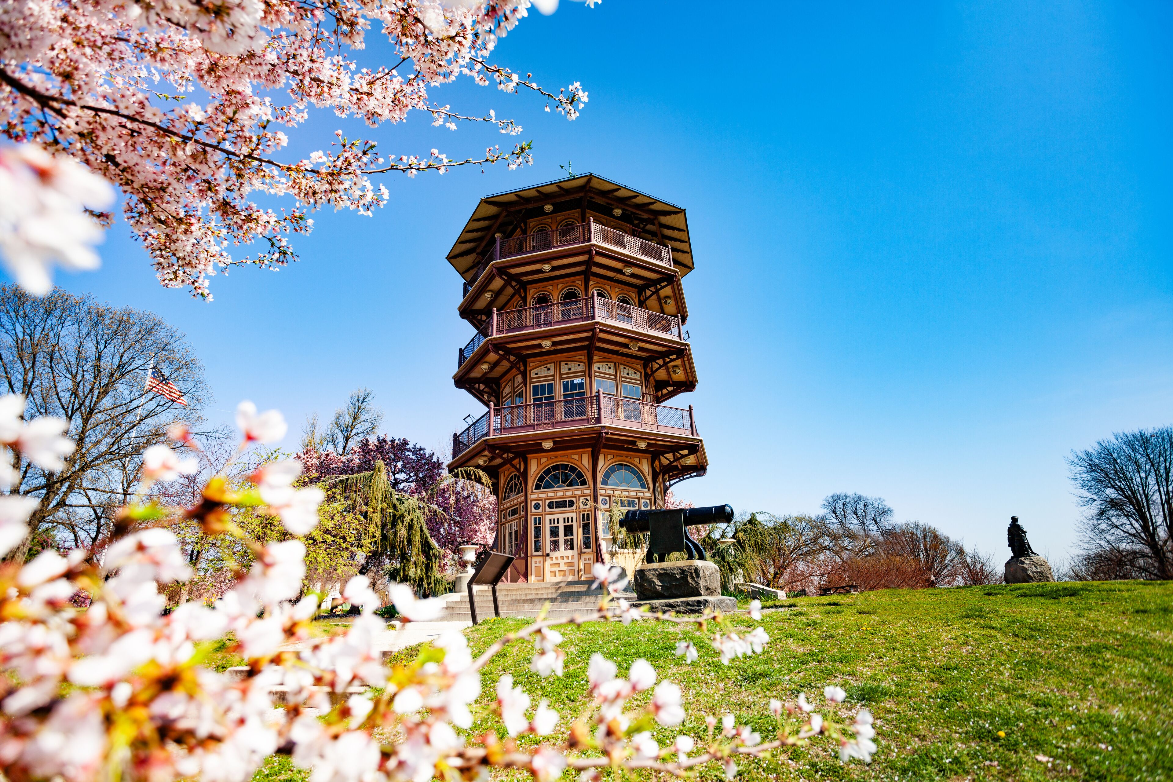A multi-tiered tower with balconies, surrounded by blooming cherry blossoms and a statue.