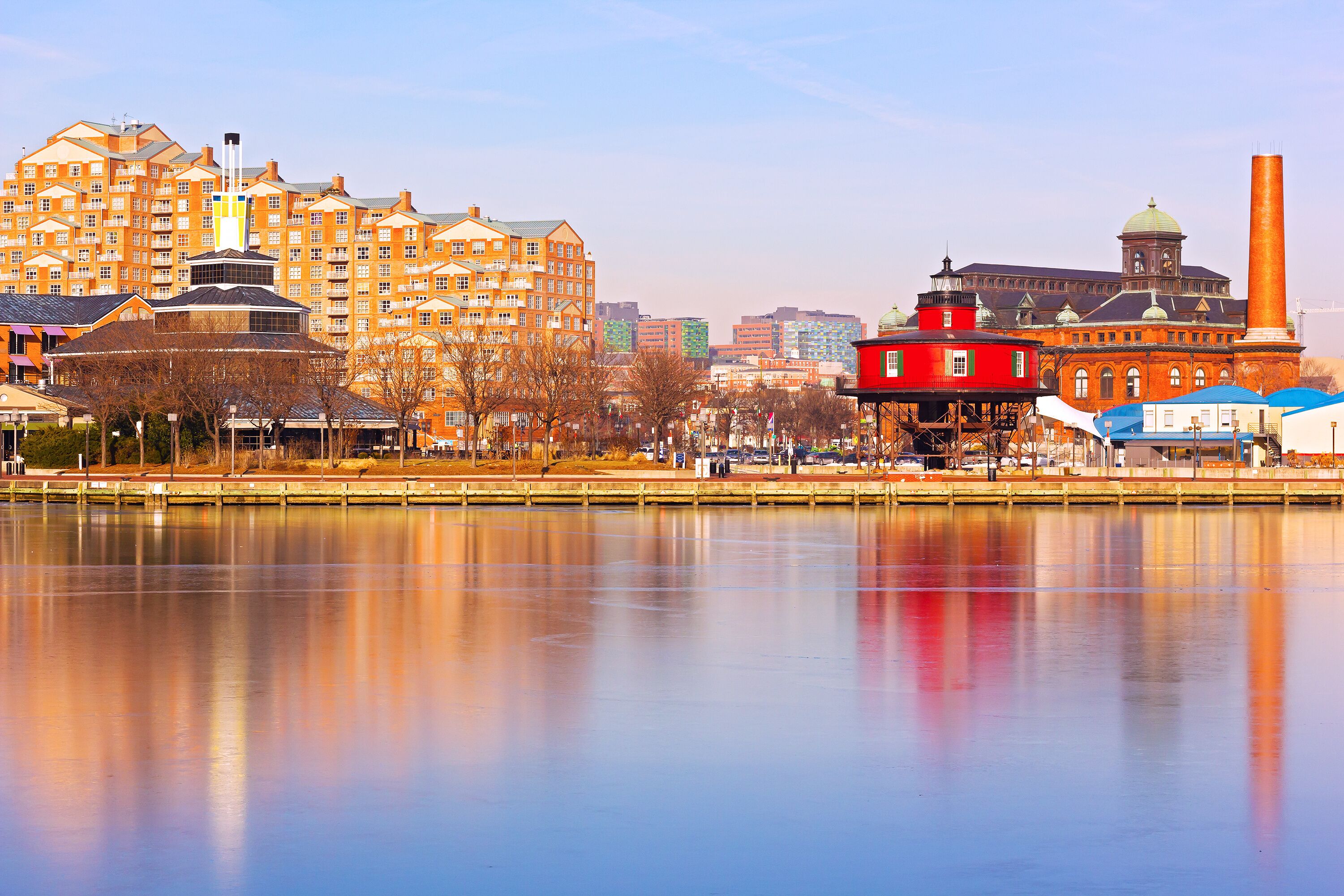 A waterfront cityscape with a prominent red building, a large industrial chimney, and modern apartment buildings.