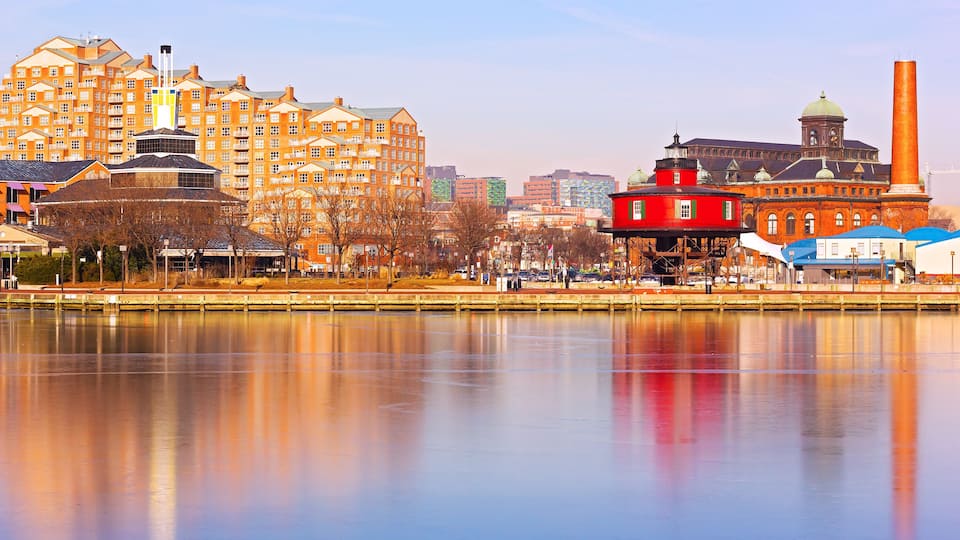 A waterfront cityscape with a prominent red building, a large industrial chimney, and modern apartment buildings.