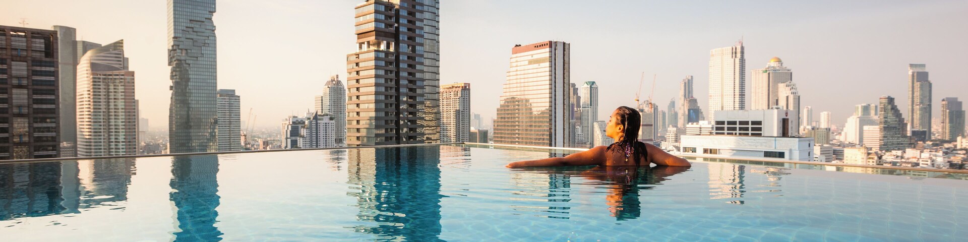 Eine Person entspannt sich in einem Pool, im Hintergrund eine Stadtansicht.
