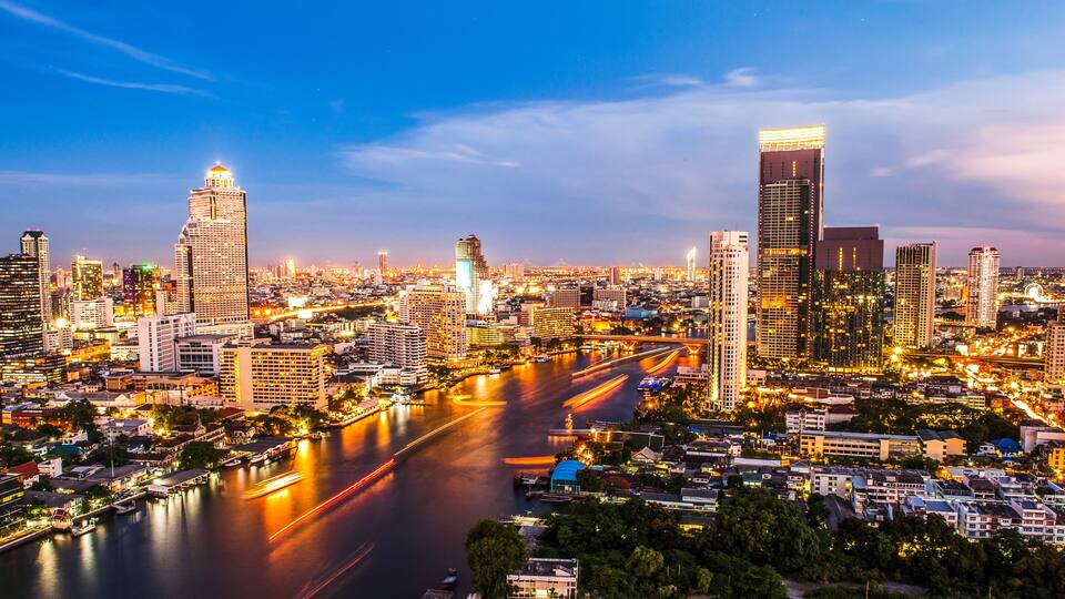 A cityscape with a river, illuminated buildings, and a prominent skyscraper.