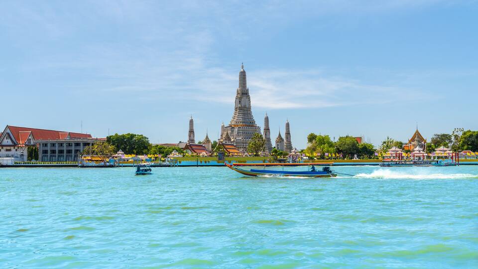 A river with boats, a temple, and buildings along the shore.