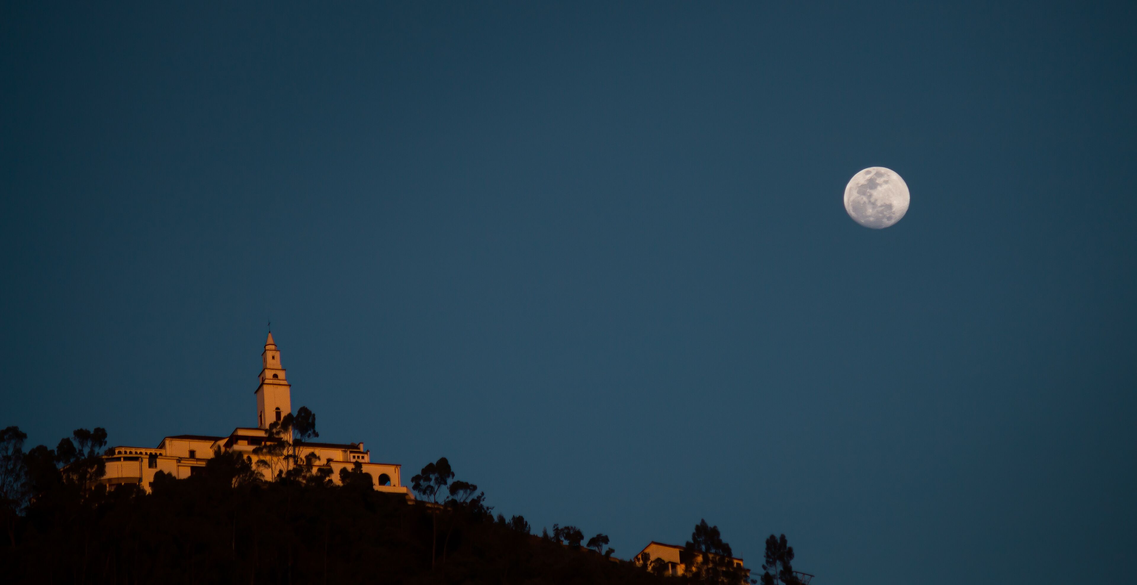 A moonlit night sky with a prominent full moon and a building with a tower silhouetted against it.