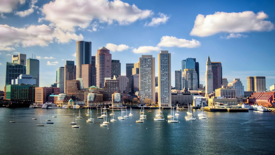 A city skyline with numerous high-rise buildings and a marina filled with sailboats.