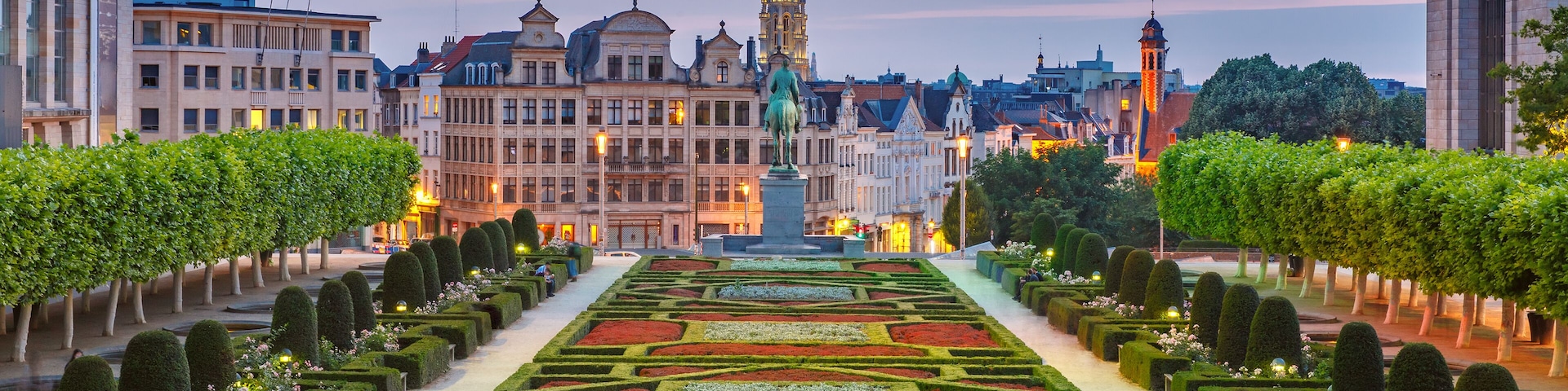 A formal garden with geometric patterns, a prominent tower, and classical architecture in the background.