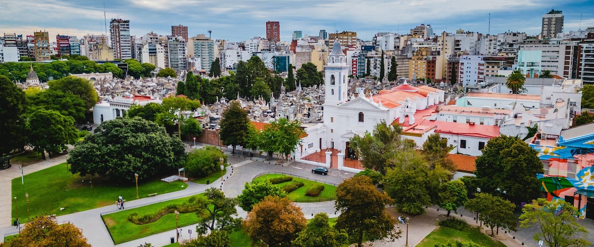 A cityscape with a prominent white church, green parks, and a mix of modern and historic buildings.