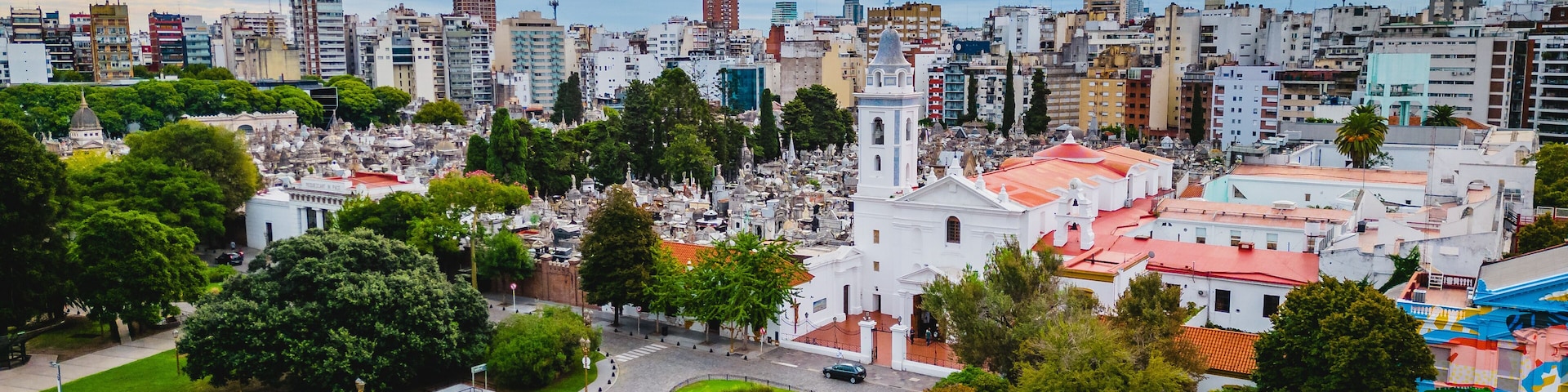 A cityscape with a prominent white church, green parks, and a mix of modern and historic buildings.