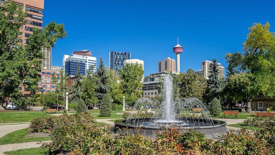 A park with a fountain, surrounded by trees and buildings.