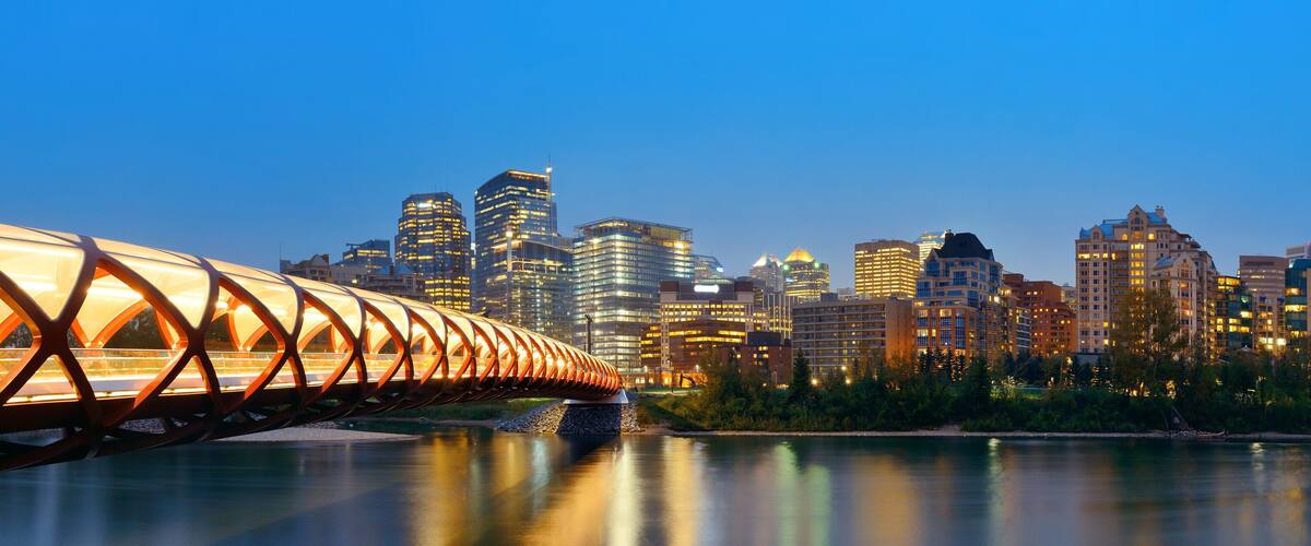 A bridge with a unique design over a river, with a city skyline in the background.