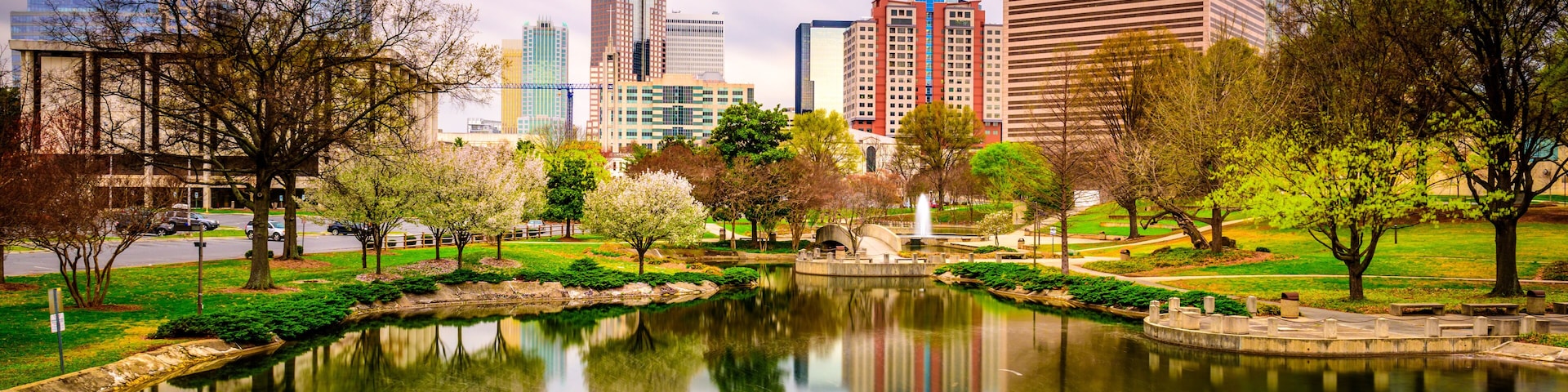 Paisagem urbana com arranha-céus modernos, um parque central com lago e céu claro.