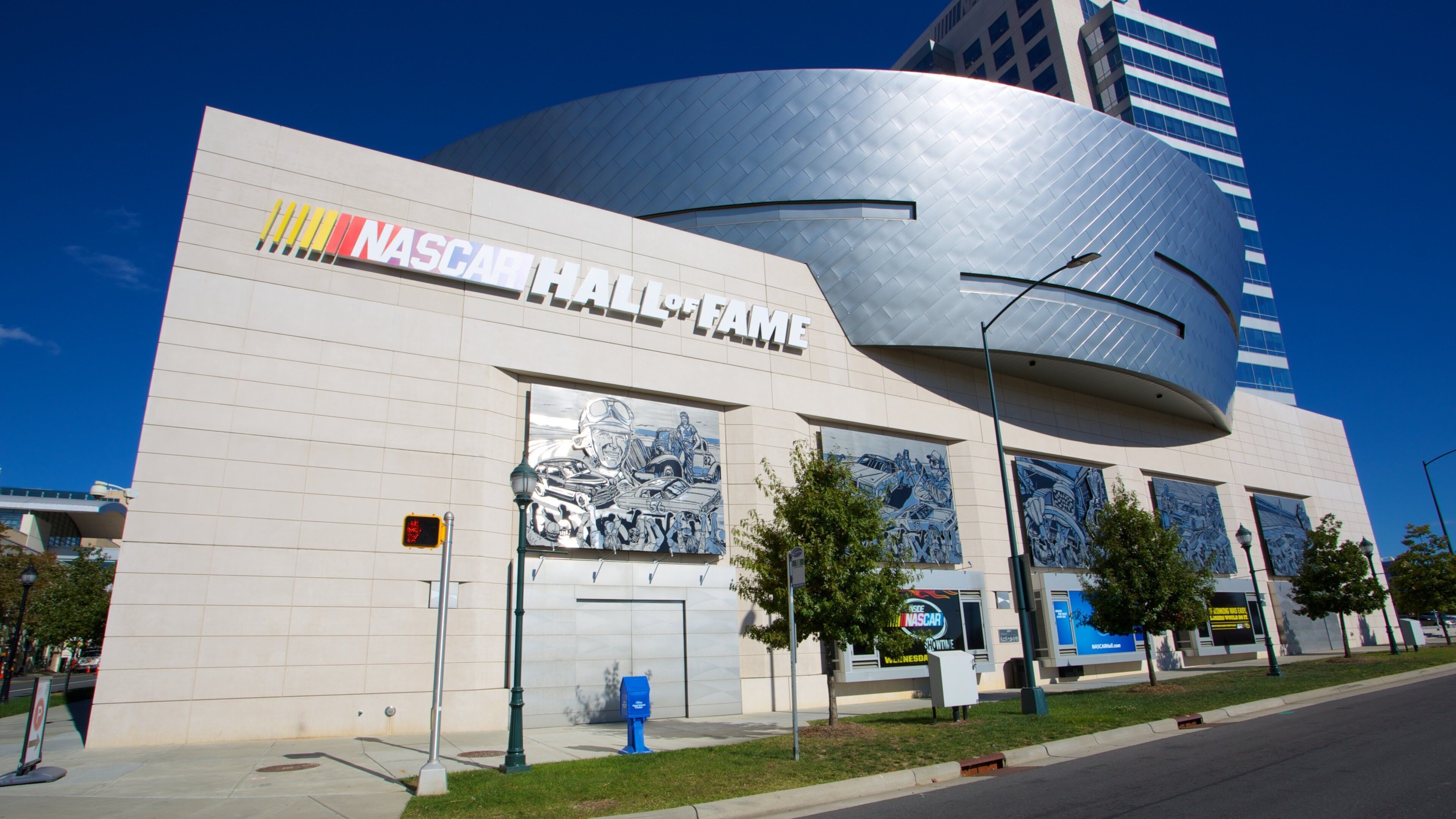 The exterior of the NASCAR Hall of Fame building with a curved metallic facade and large murals on the side.