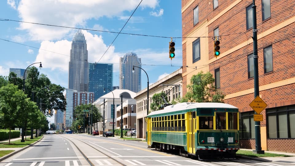 A trolley on a street with a brick building, a green traffic light, and tall buildings in the background.
