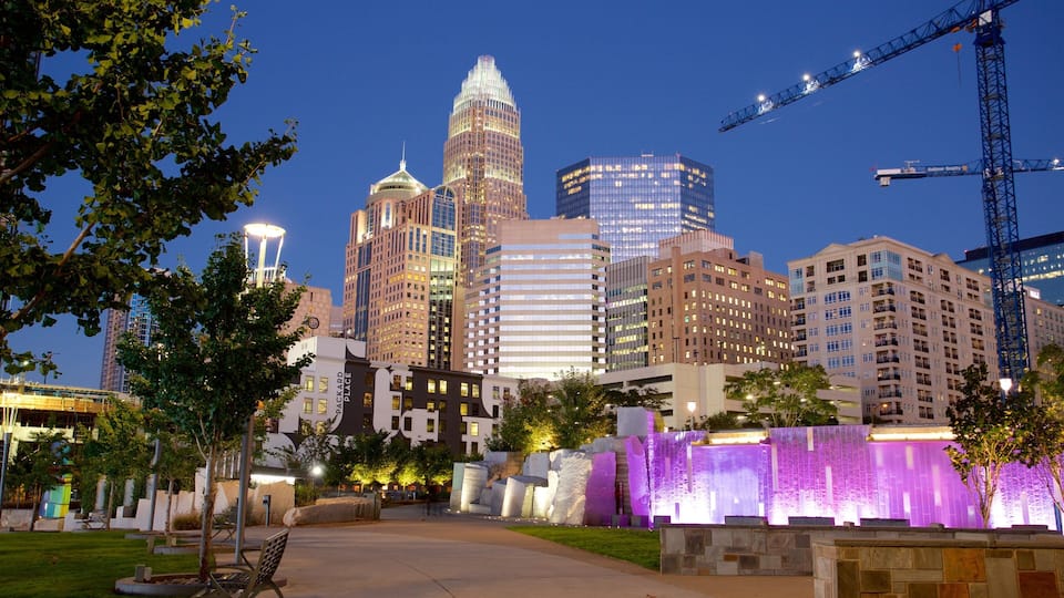 A city skyline with modern buildings, a park with a fountain, and a construction crane in the background.