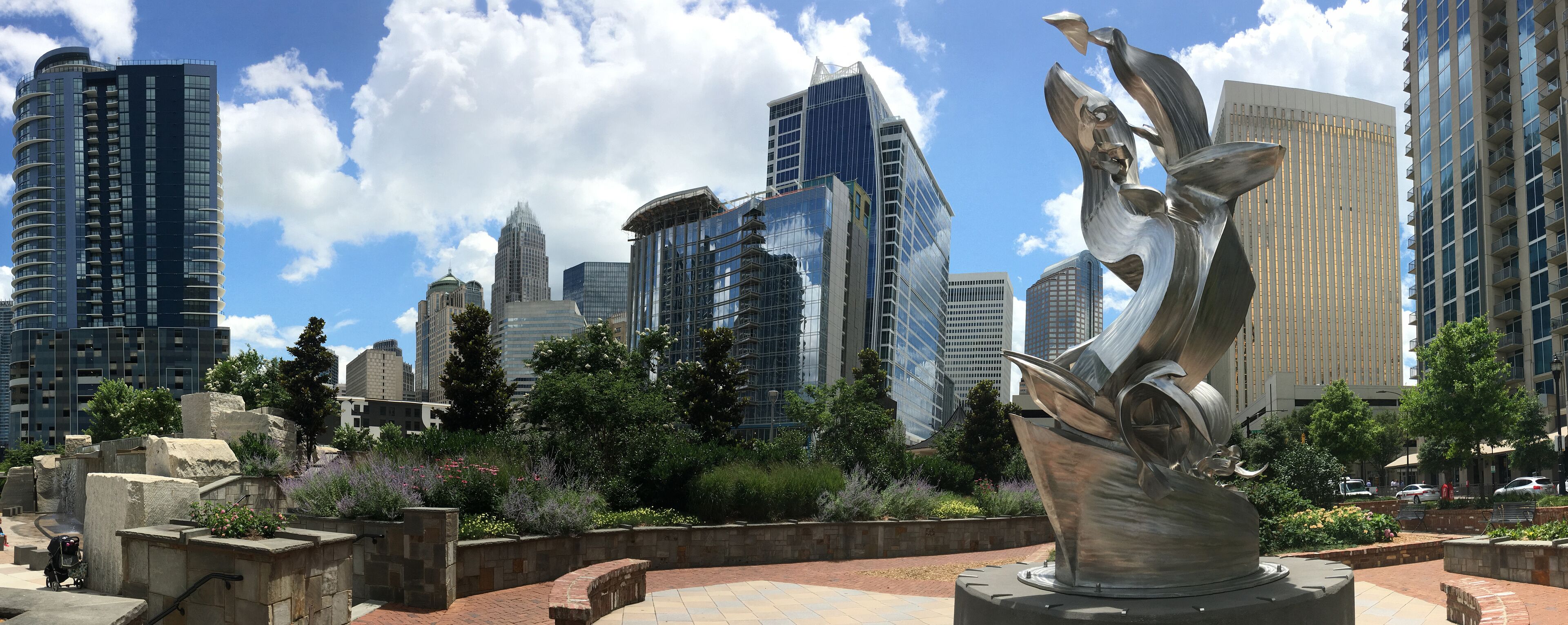 A sculpture in a park with modern buildings in the background.