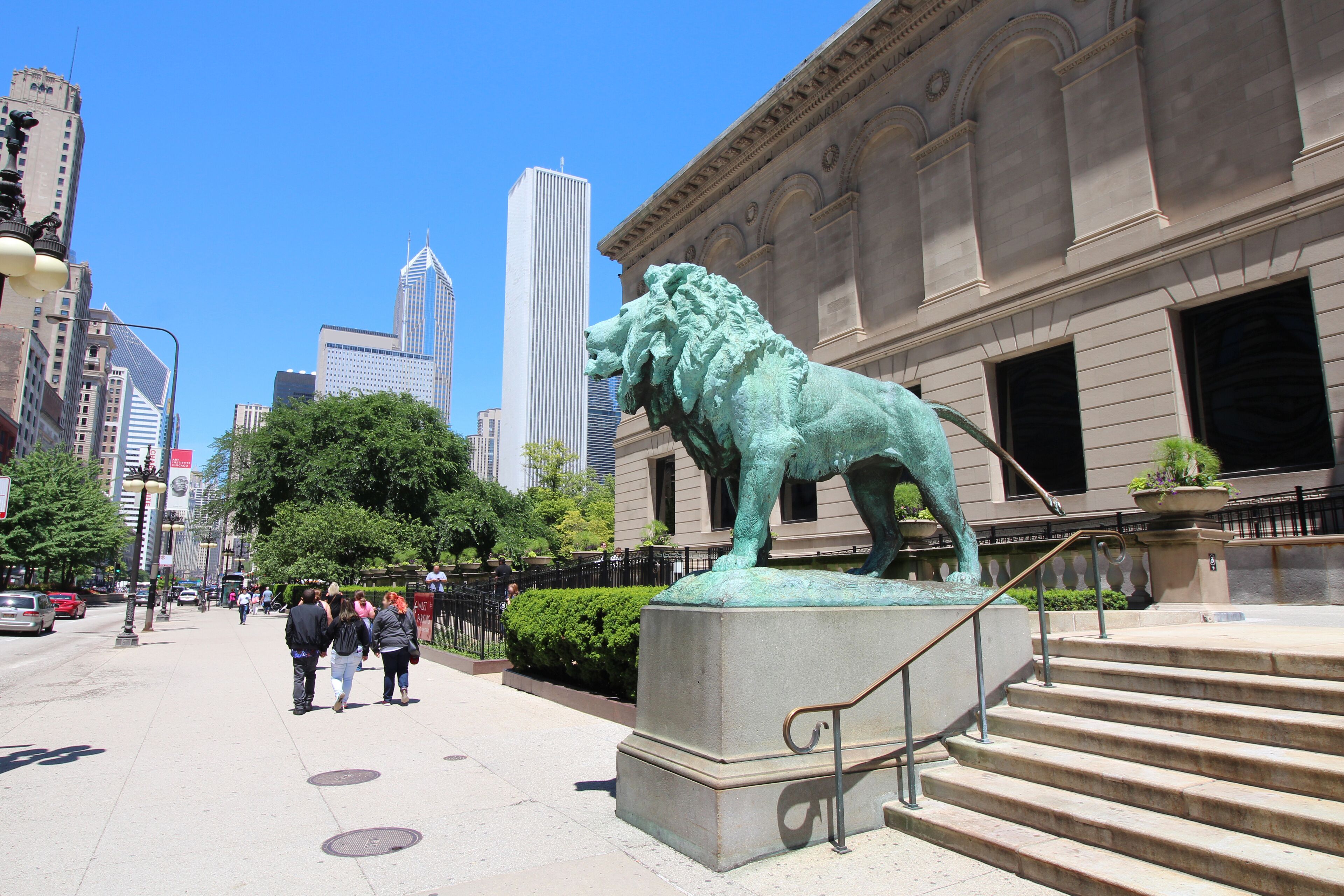 A bronze lion statue in front of a classical building with steps leading up to it.