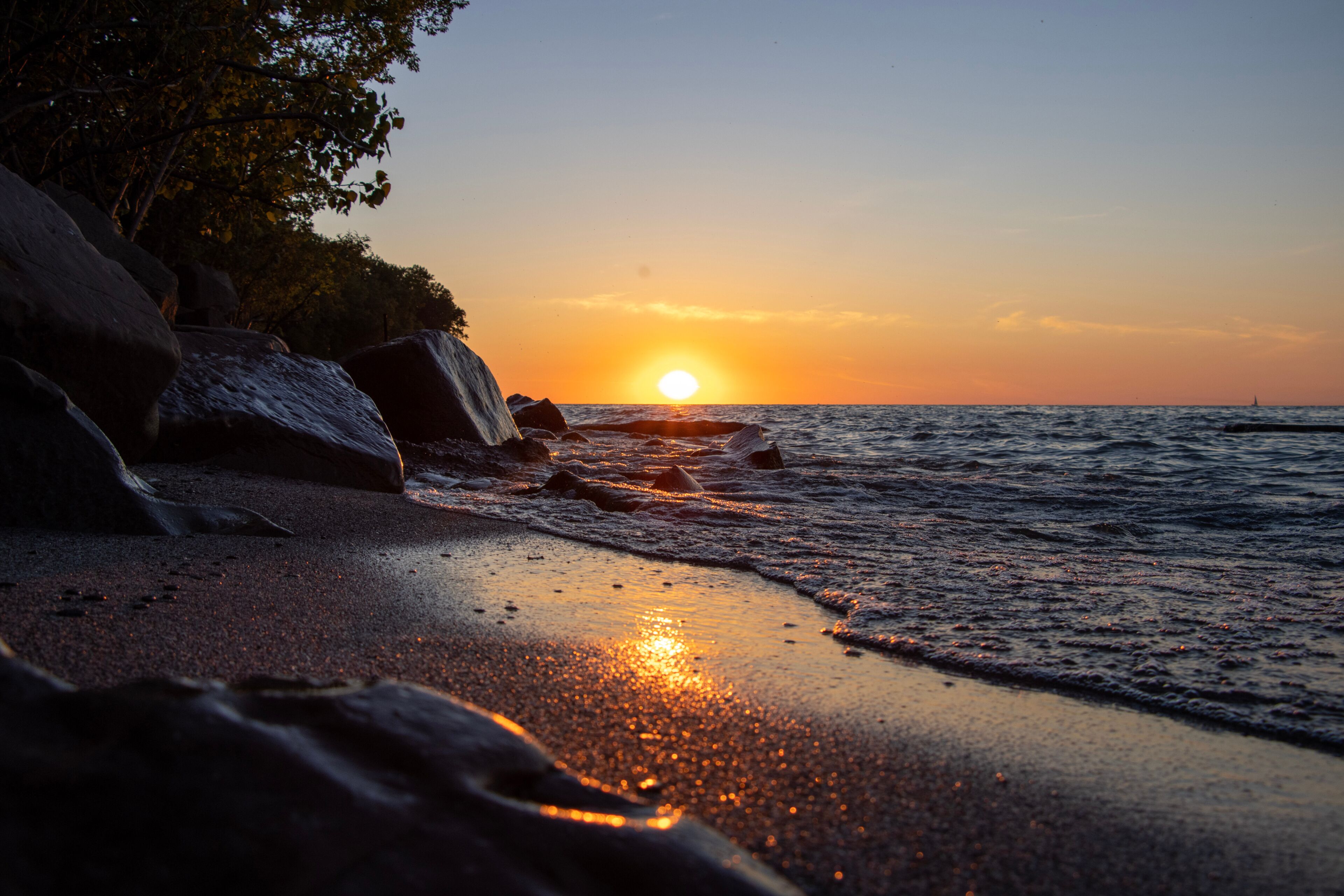 A sunset over a rocky coastline with waves gently lapping at the shore.