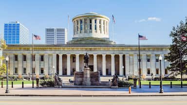 A neoclassical building with a central dome, flanked by columns, and two American flags.