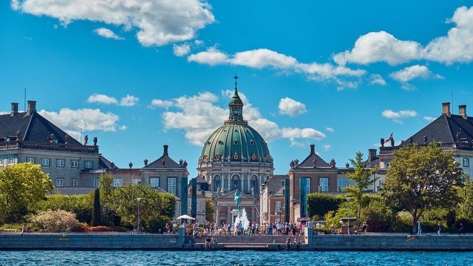 A historic building with a green dome, surrounded by trees and water.