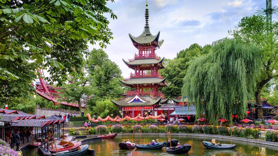 A traditional pagoda surrounded by a pond with boats and lush greenery.
