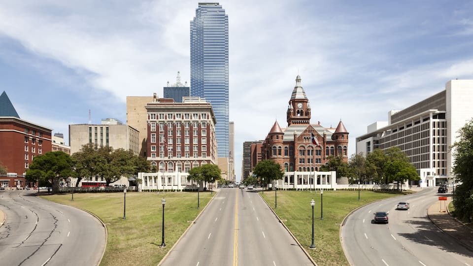 A city street with a prominent building with a clock tower, a tall skyscraper, and a historic building with a dome.
