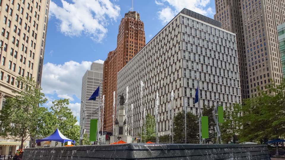 A cityscape with tall buildings, a statue, and a fountain.