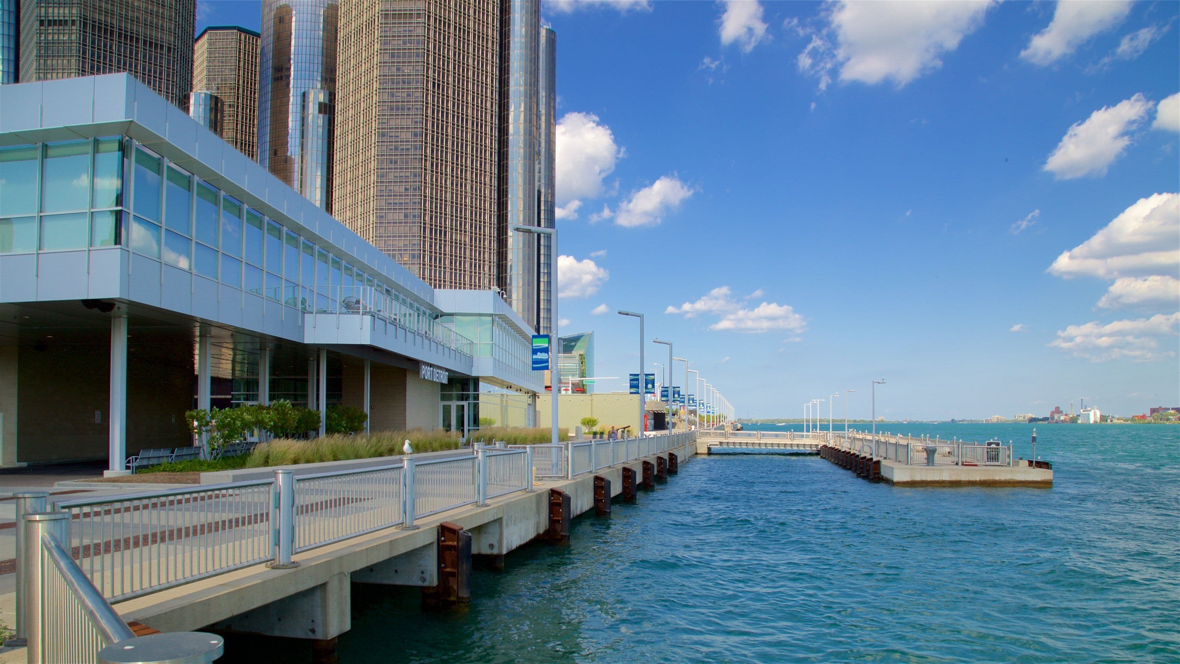 A waterfront promenade with modern buildings, a bridge, and a clear blue sky.
