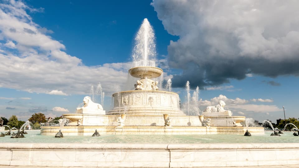 A large, multi-tiered fountain with water jets and statues under a partly cloudy sky.