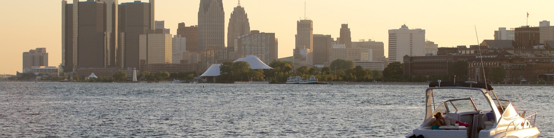 Silhueta urbana ao pôr do sol, com um barco na água.