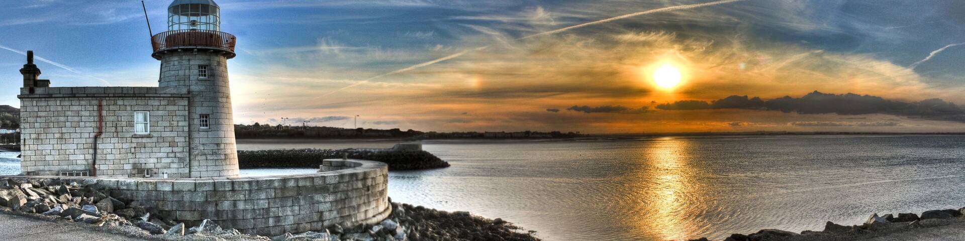 A lighthouse by a calm sea at sunset with a clear sky.