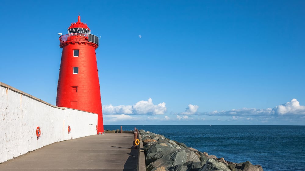 Un phare rouge au bord de la mer, avec un mur blanc et une côte rocheuse.