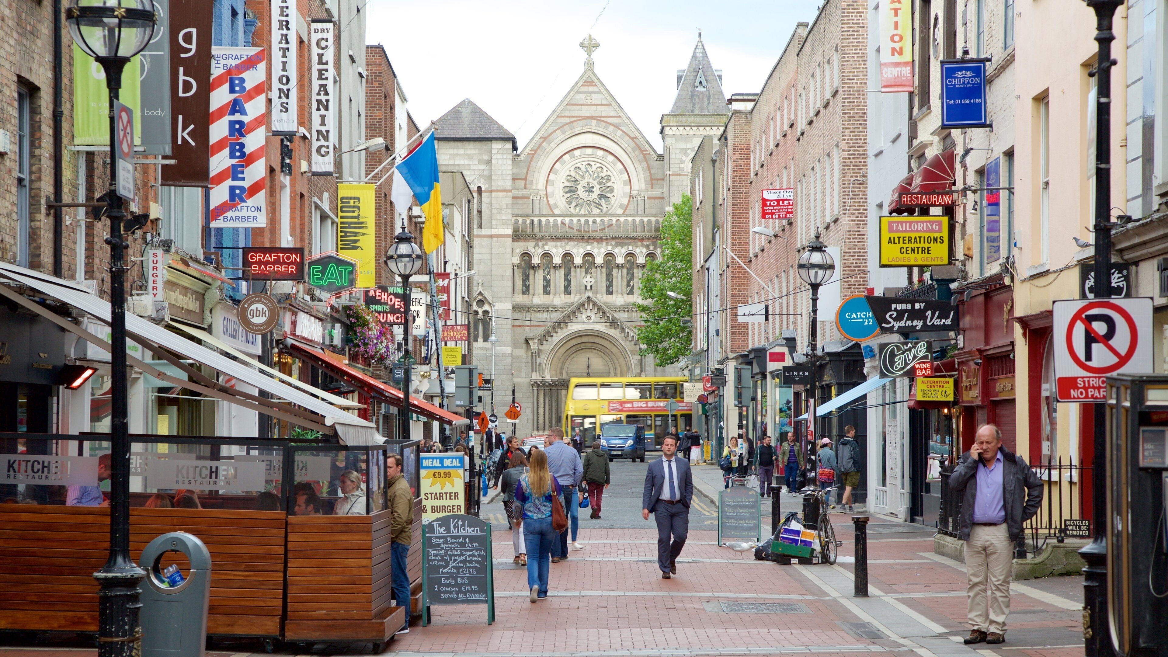 A busy street with shops, a double-decker bus, and a historic building with a clock tower.