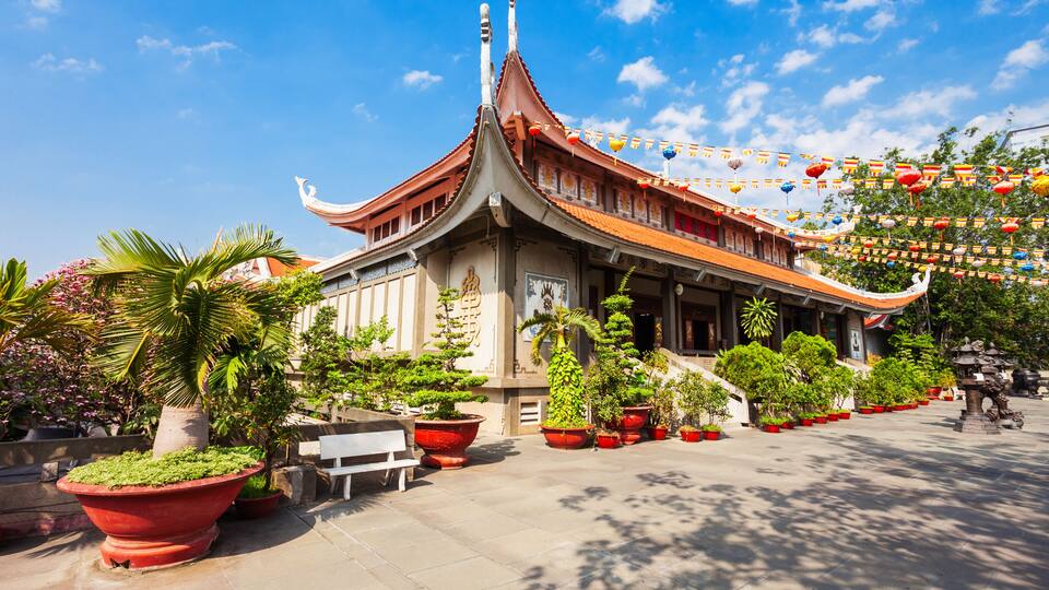 A traditional temple with a curved roof, surrounded by potted plants and a clear blue sky.