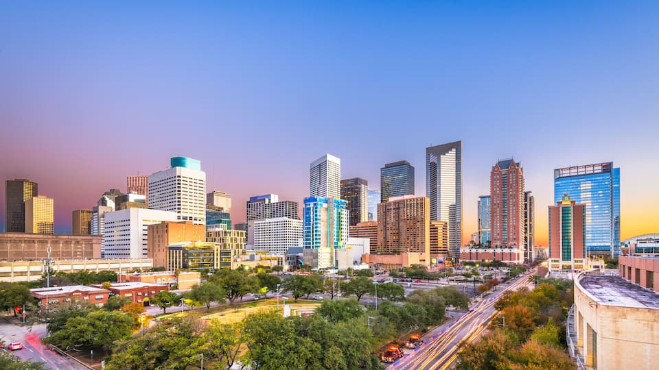 A city skyline with modern high-rise buildings, a network of roads, and surrounding greenery.