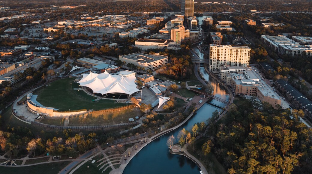 An aerial view of a cityscape with a prominent white-roofed stadium, a river, and surrounding buildings.