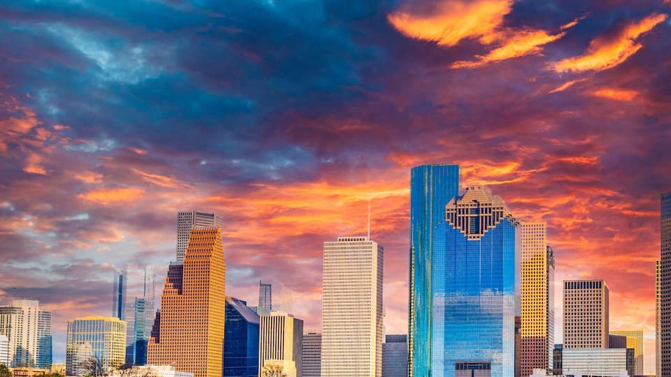A city skyline with modern skyscrapers under a colorful sunset sky.