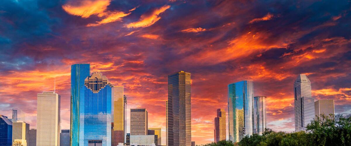 A city skyline with modern skyscrapers under a colorful sunset sky.