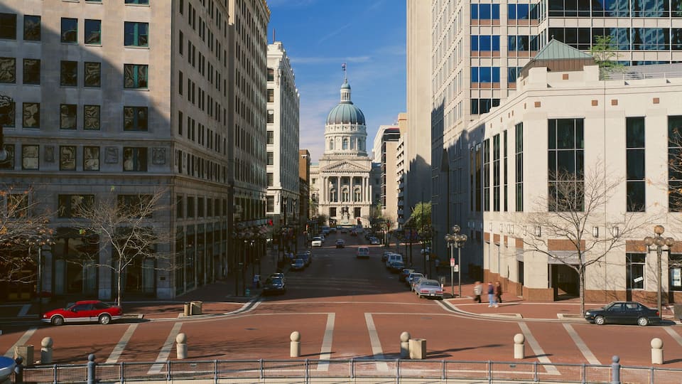 A city street with historic buildings, a red car, and a blue car parked along the road.