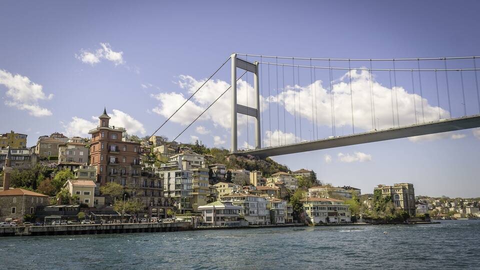 A bridge spanning a body of water with buildings on the opposite shore.