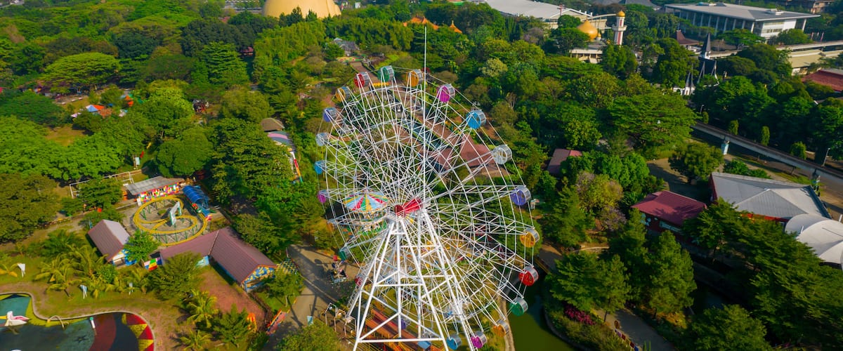 A large Ferris wheel surrounded by lush greenery and various buildings.