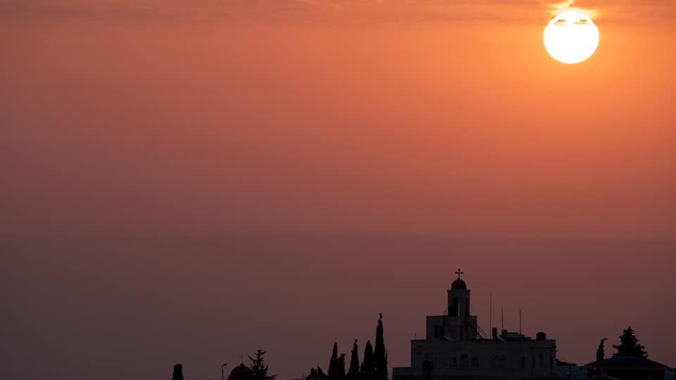 Ein Sonnenuntergang über einer Stadtlandschaft mit einer markanten Kirche und umliegenden Gebäuden.