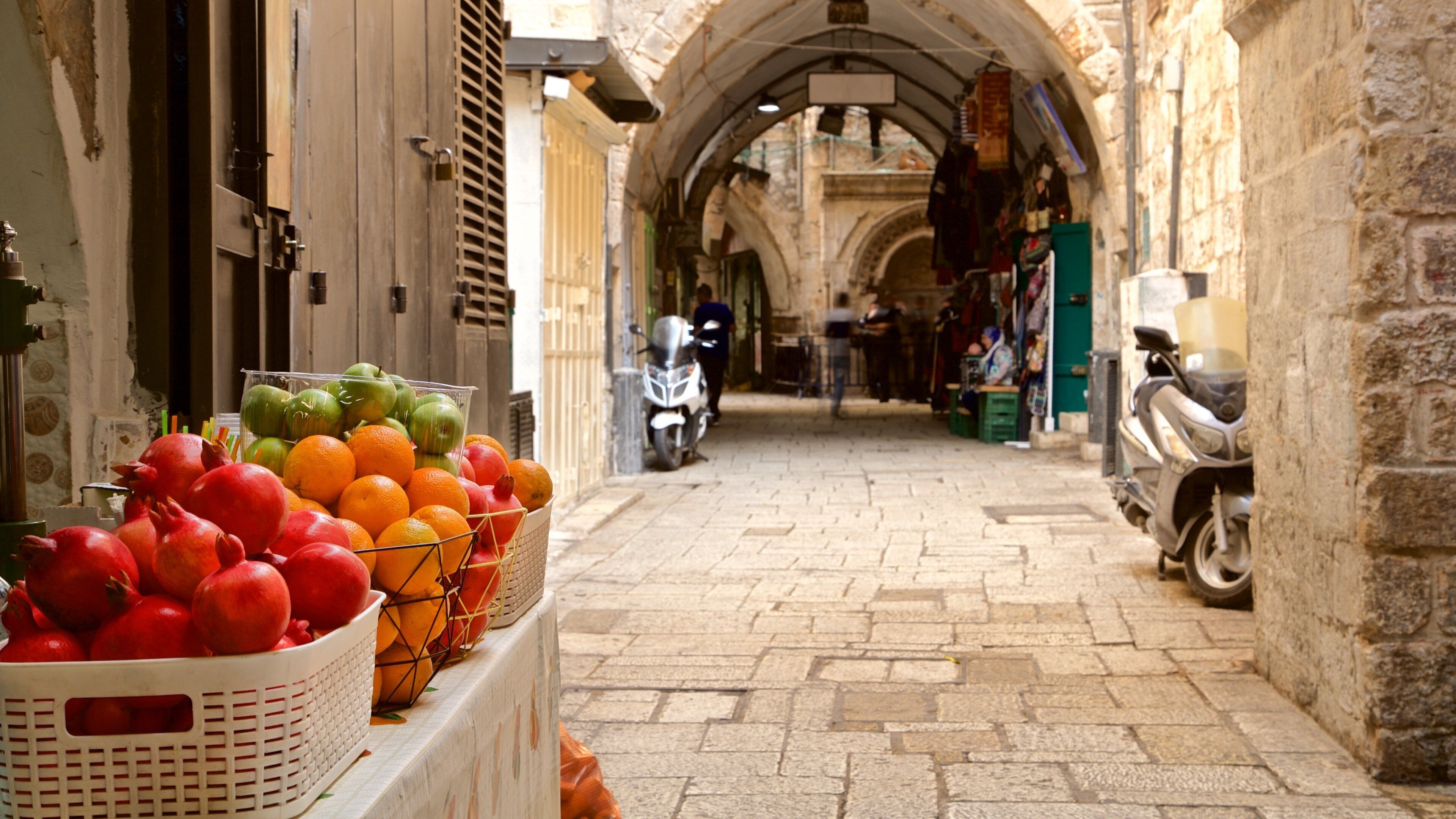 Una calle estrecha con cestas de fruta a la izquierda y una moto a la derecha.
