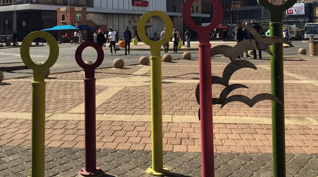 One end of Ghandi Square. There are bus stops on both sides, a statue of Ghandi, and plenty of shops.